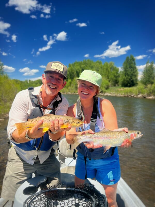 Two happy anglers holding their catches, a brown trout and a rainbow trout, during a half-day walk and wade trip.