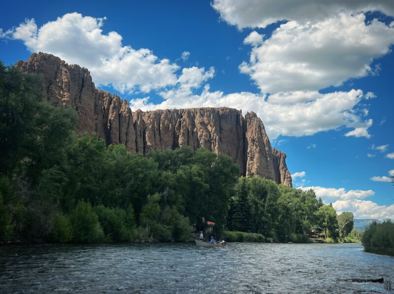 Boat drifting on a picturesque river surrounded by towering cliffs and overcast skies.